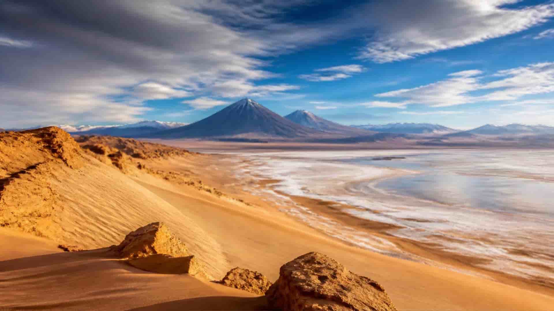 Vast dunes and salt flats of the Atacama Desert in Chile stretch toward distant Andes volcanoes under a dramatic desert sky.