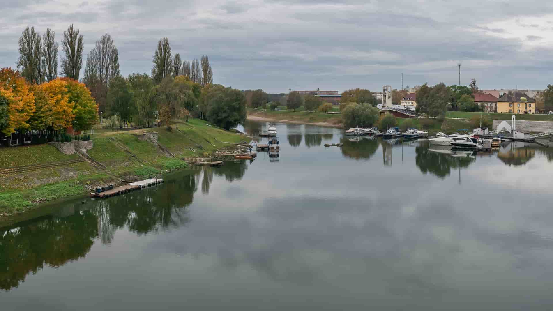The Sugovica river marina in Baja, Hungary, with moored boats, autumn-colored trees and town buildings reflected in the calm waterfront.