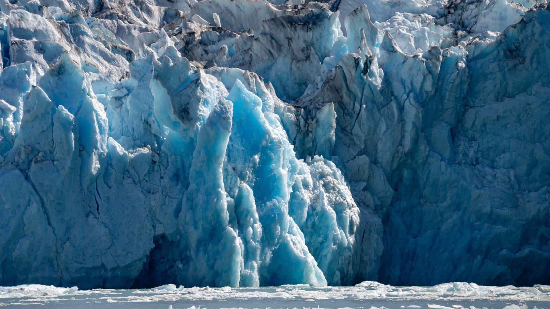 Towering blue ice formations of Dawes Glacier in Endicott Arm, Alaska, with jagged crevasses and floating ice fragments above calm glacial water, showcasing the dramatic scenery of this iconic Alaska fjord.