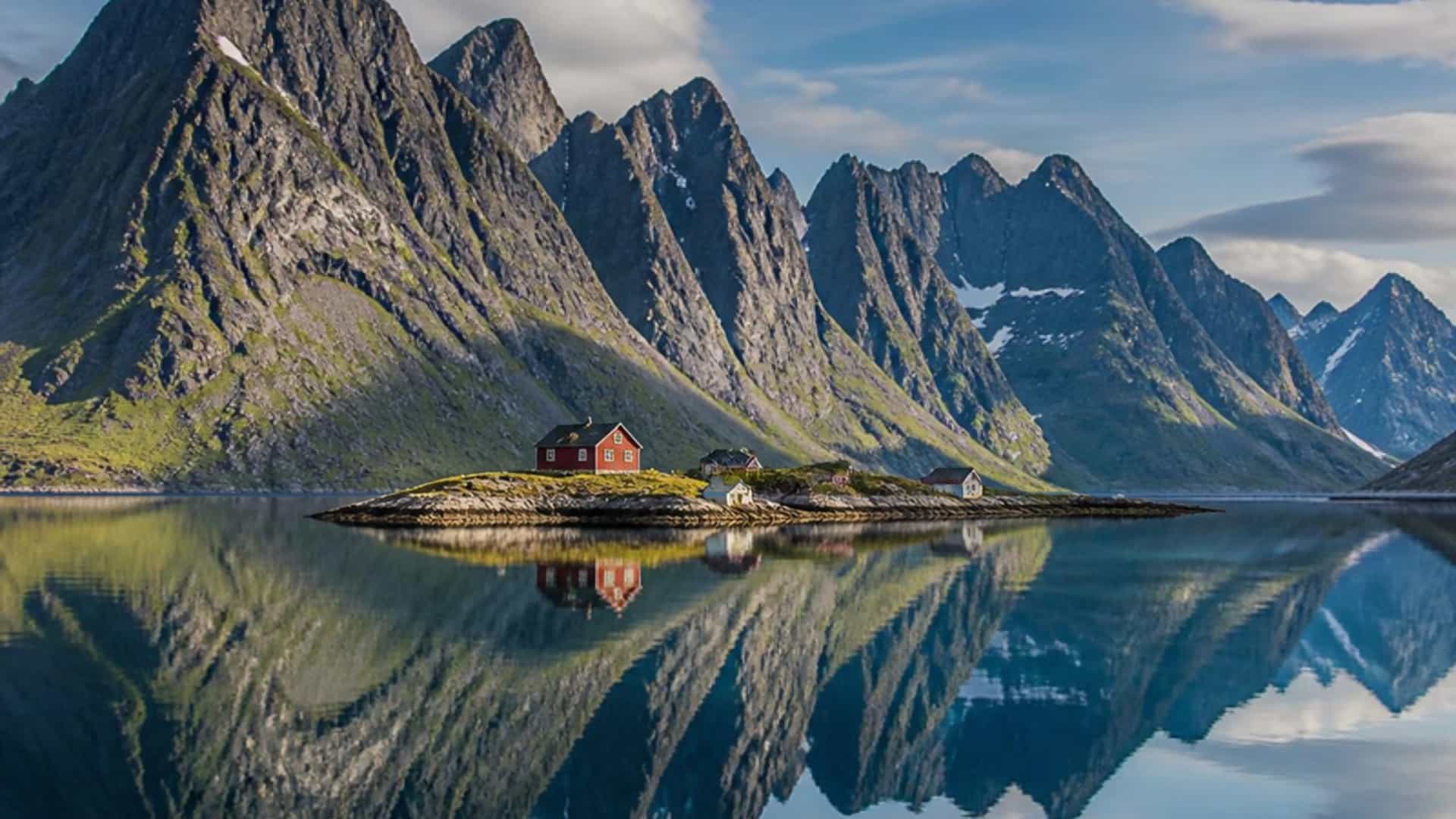 The remote Arctic islet of Nordfjordholmen in Nordland, Norway, with dramatic peaks reflected in still fjord water.