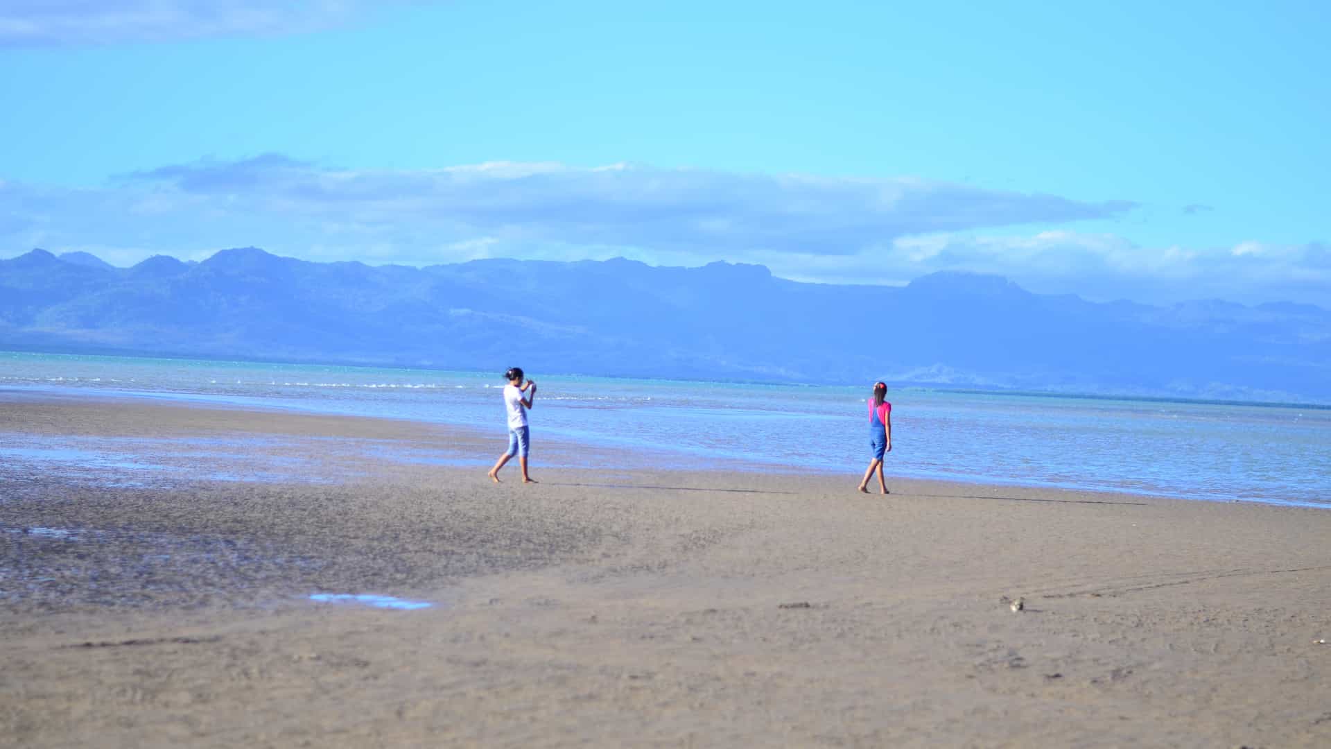 A tranquil tropical beach near Kupang, Indonesia, with soft sand, calm turquoise water and hazy mountains on the horizon.