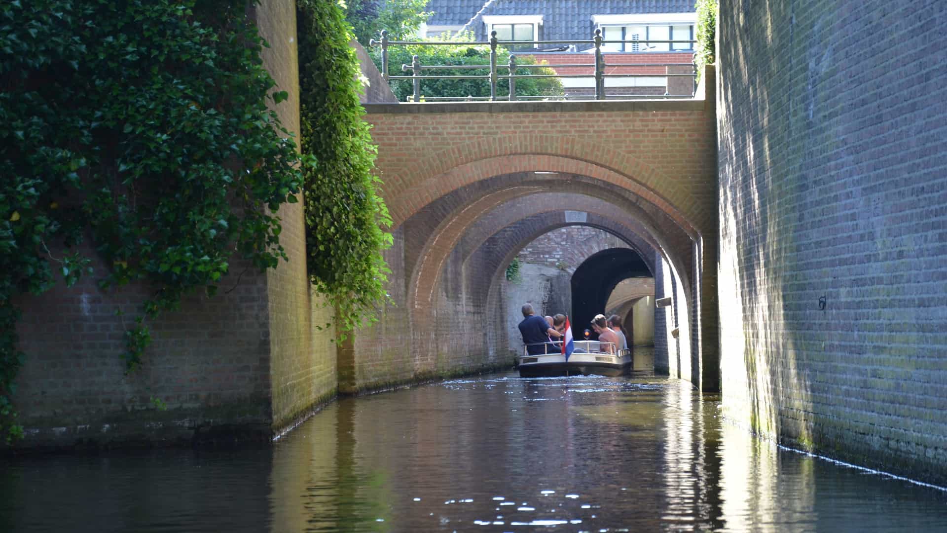 A tour boat glides through the brick-arched Binnendieze canal beneath the historic streets of s-Hertogenbosch, Netherlands.