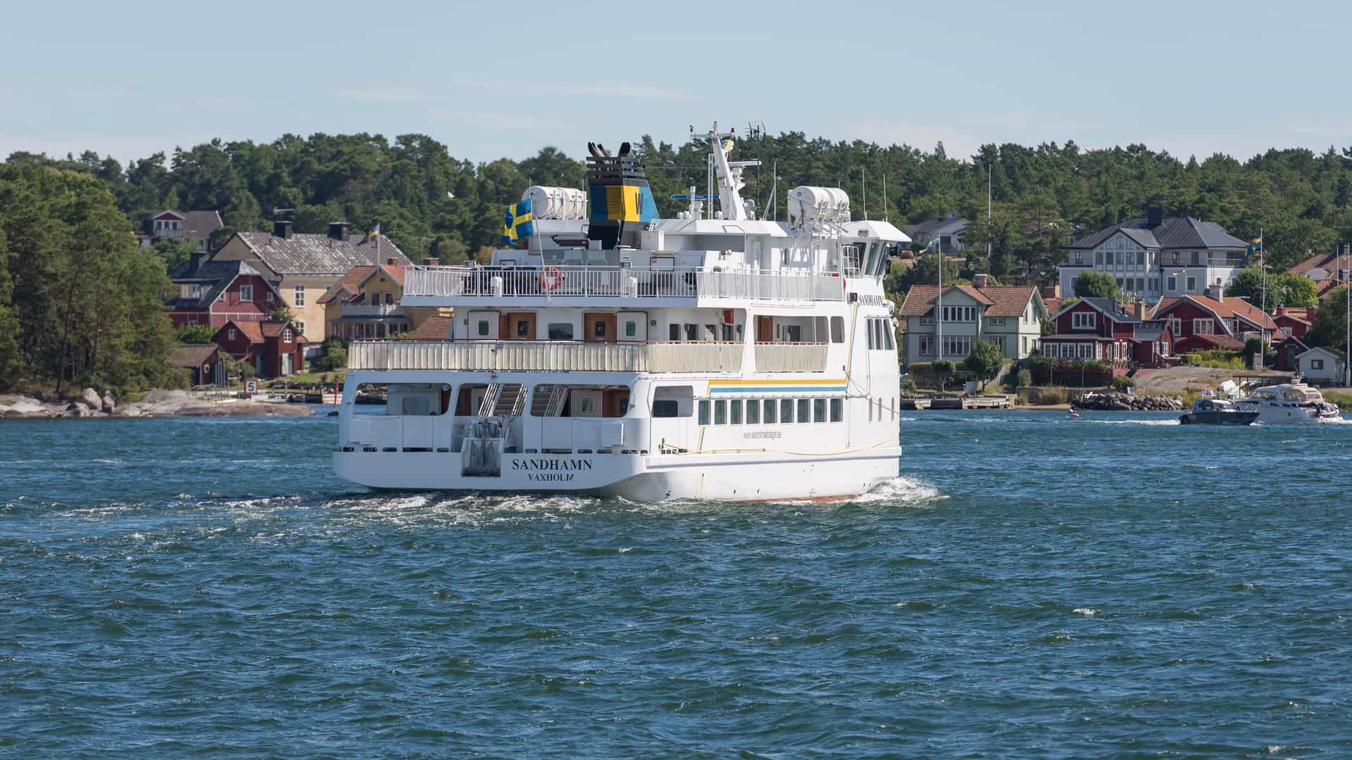 The Sandhamn ferry departs the picturesque Stockholm archipelago harbor, with classic wooden houses and pine forest along the shore.
