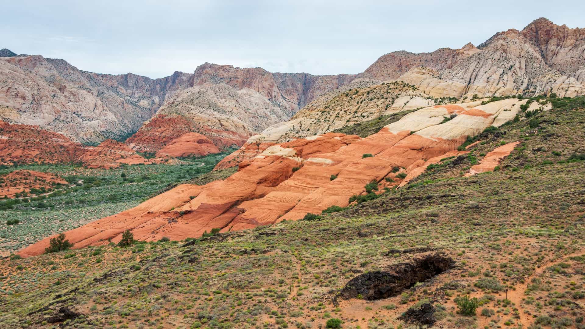 A wide view of red and cream sandstone cliffs and desert slopes in Snow Canyon State Park, Utah.
