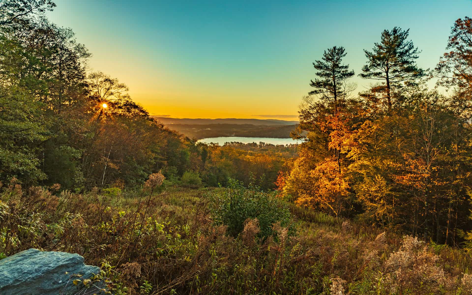 A sunset view over a distant lake in Stockbridge, Massachusetts, framed by autumn-colored trees.