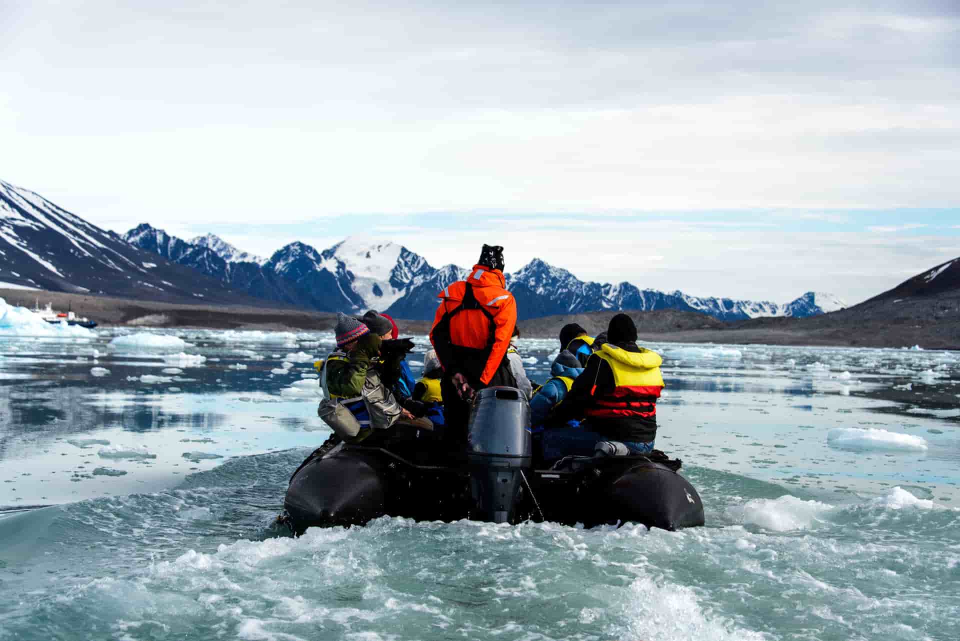 Jagged, snow-dusted mountain peaks and deep-blue glaciers rise above the tranquil icy waters of a fjord in the Arctic wilderness of Svalbard, Norway.