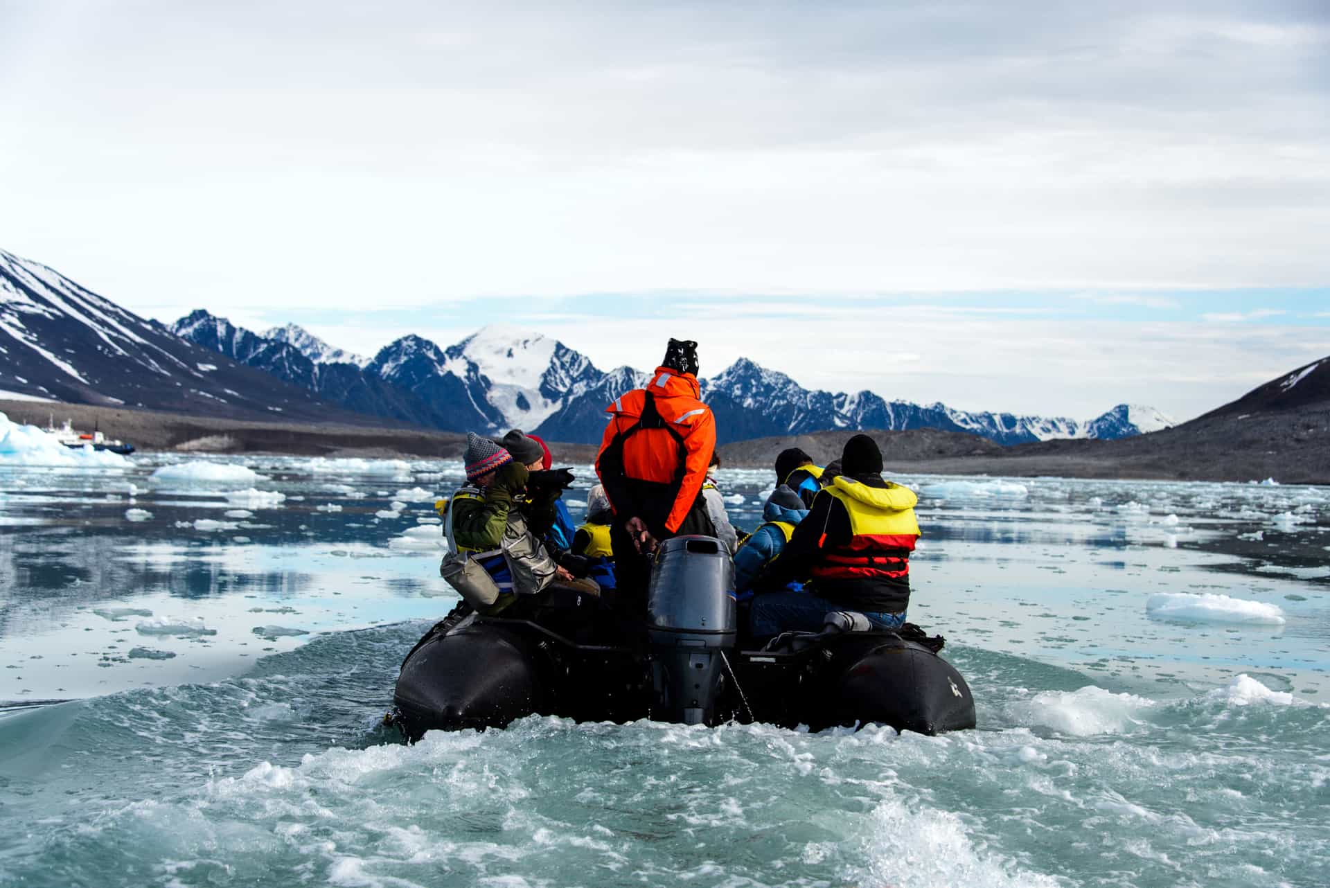 Jagged, snow-dusted mountain peaks and deep-blue glaciers rise above the tranquil icy waters of a fjord in the Arctic wilderness of Svalbard, Norway.