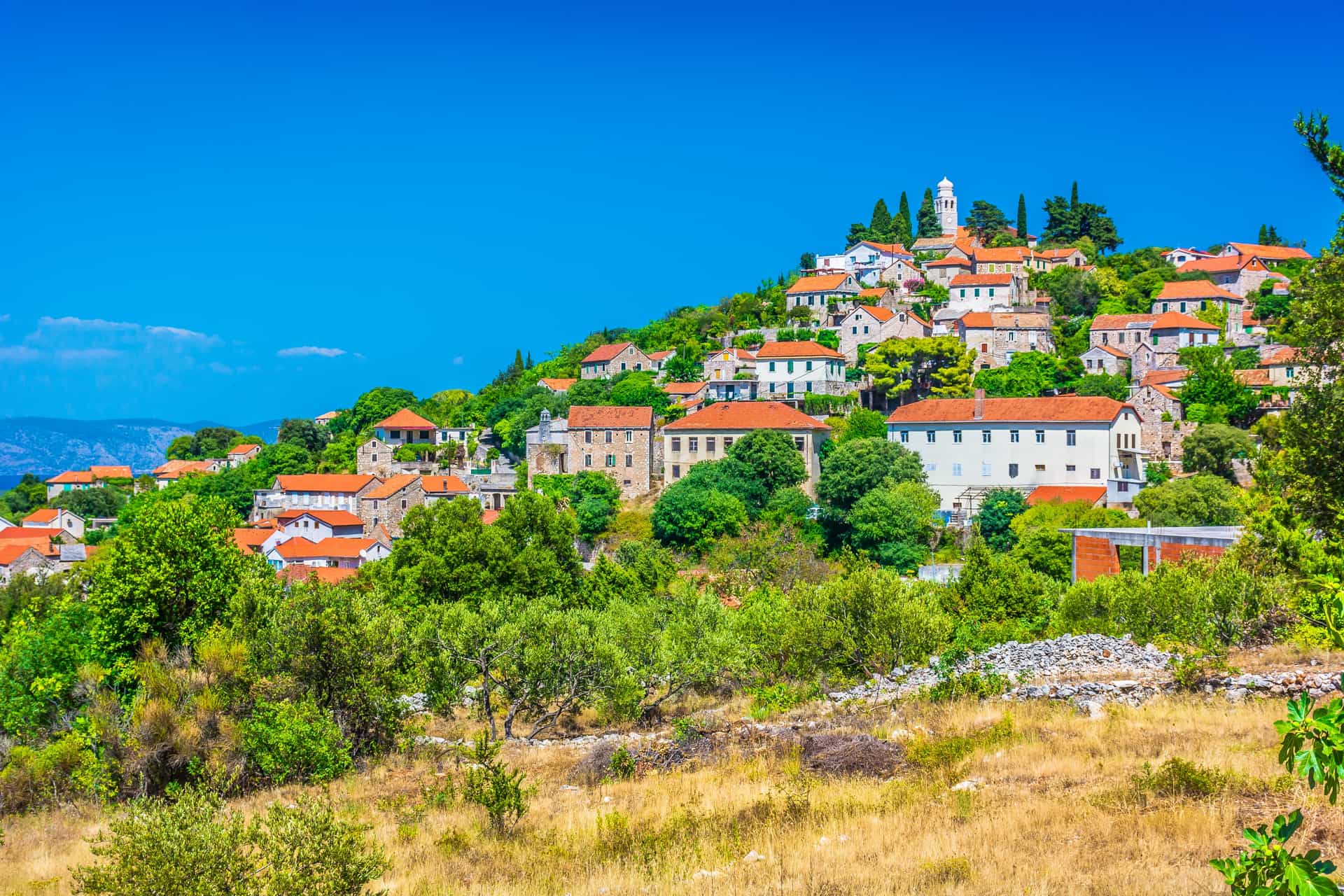 A hillside village of stone houses with red-tiled roofs and a small bell tower in Vrisnik, Croatia.