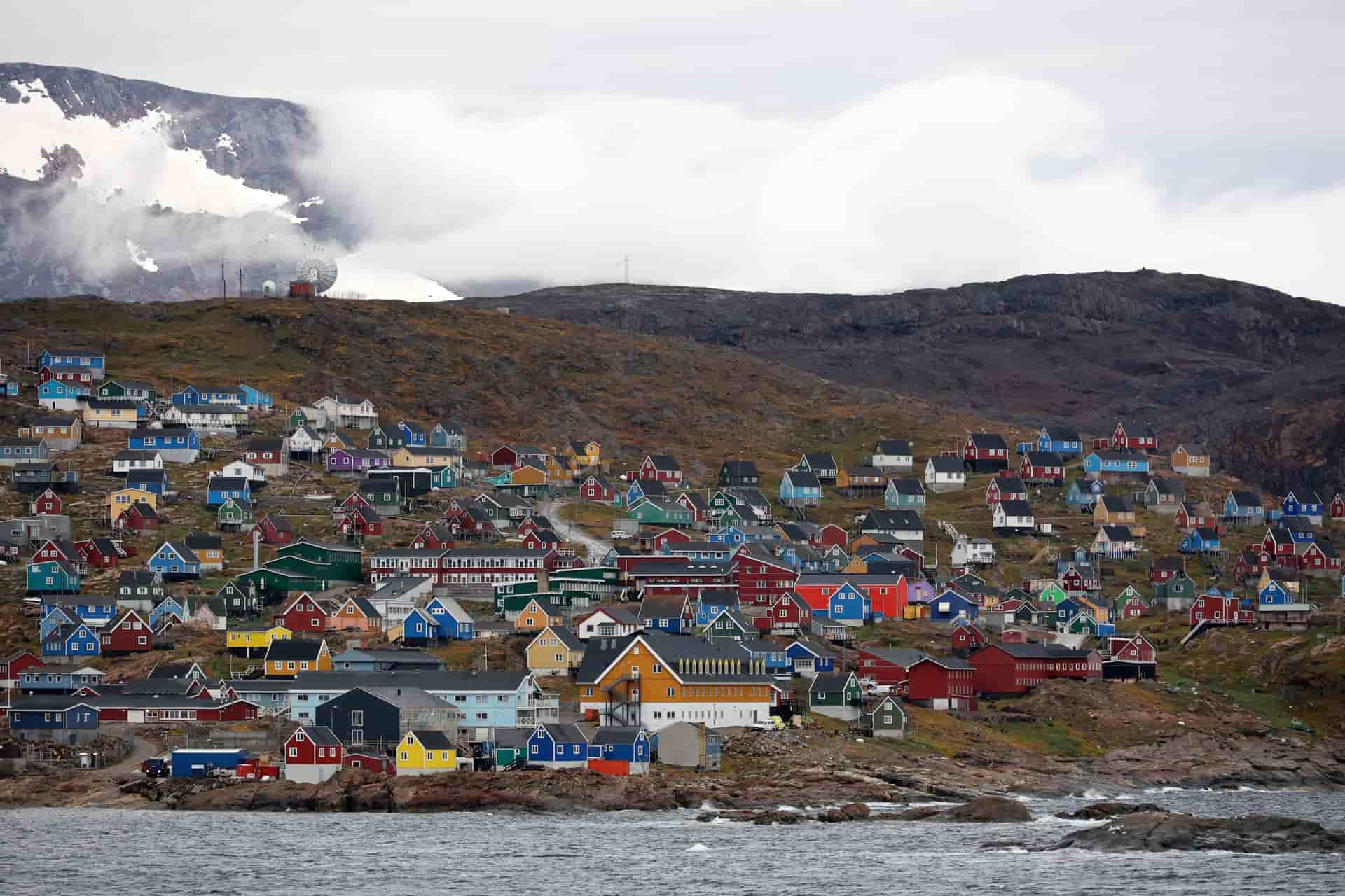 A village of brightly colored houses built into a rocky hillside along the coast of Greenland.