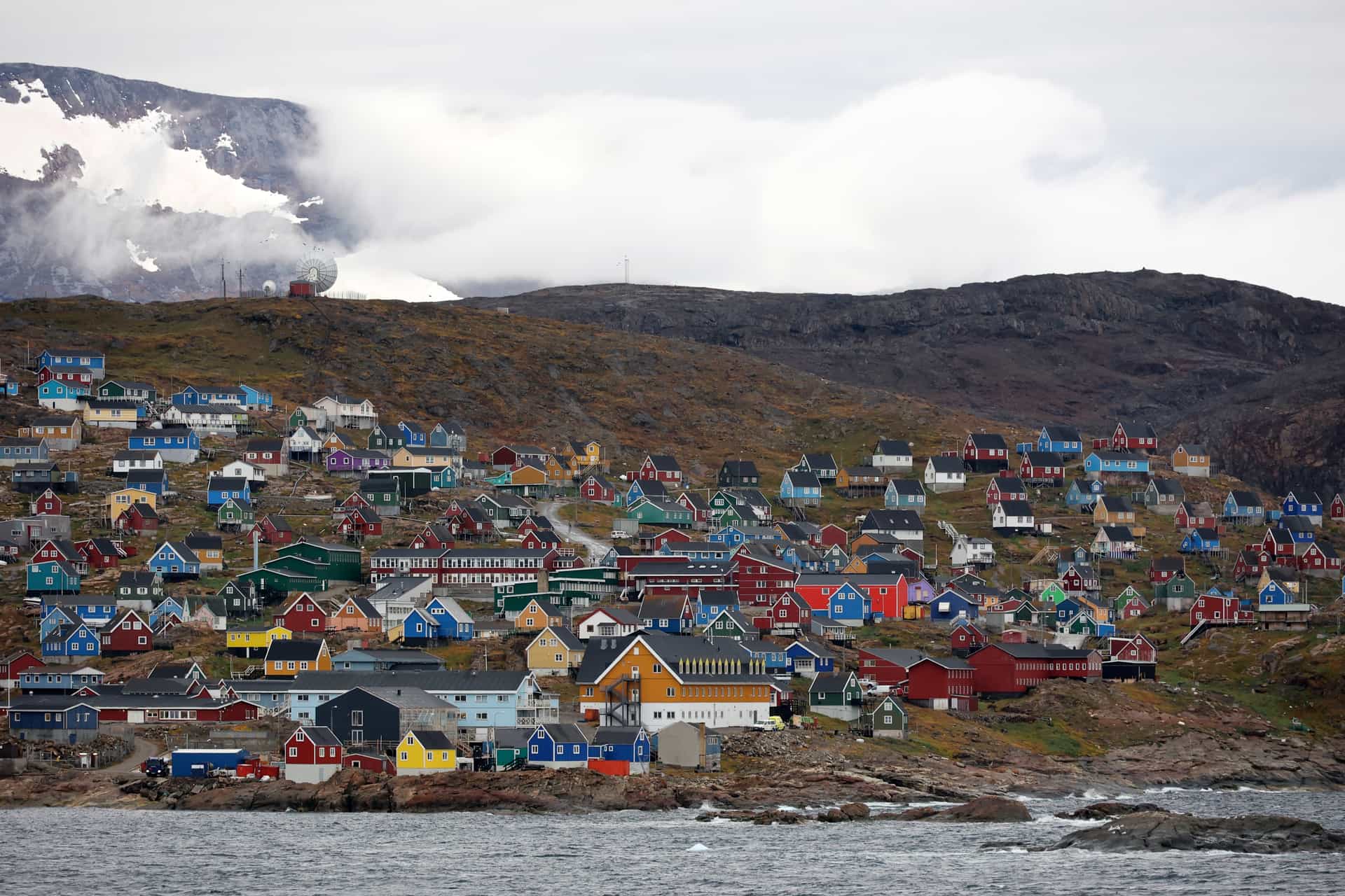 A village of brightly colored houses built into a rocky hillside along the coast of Greenland.