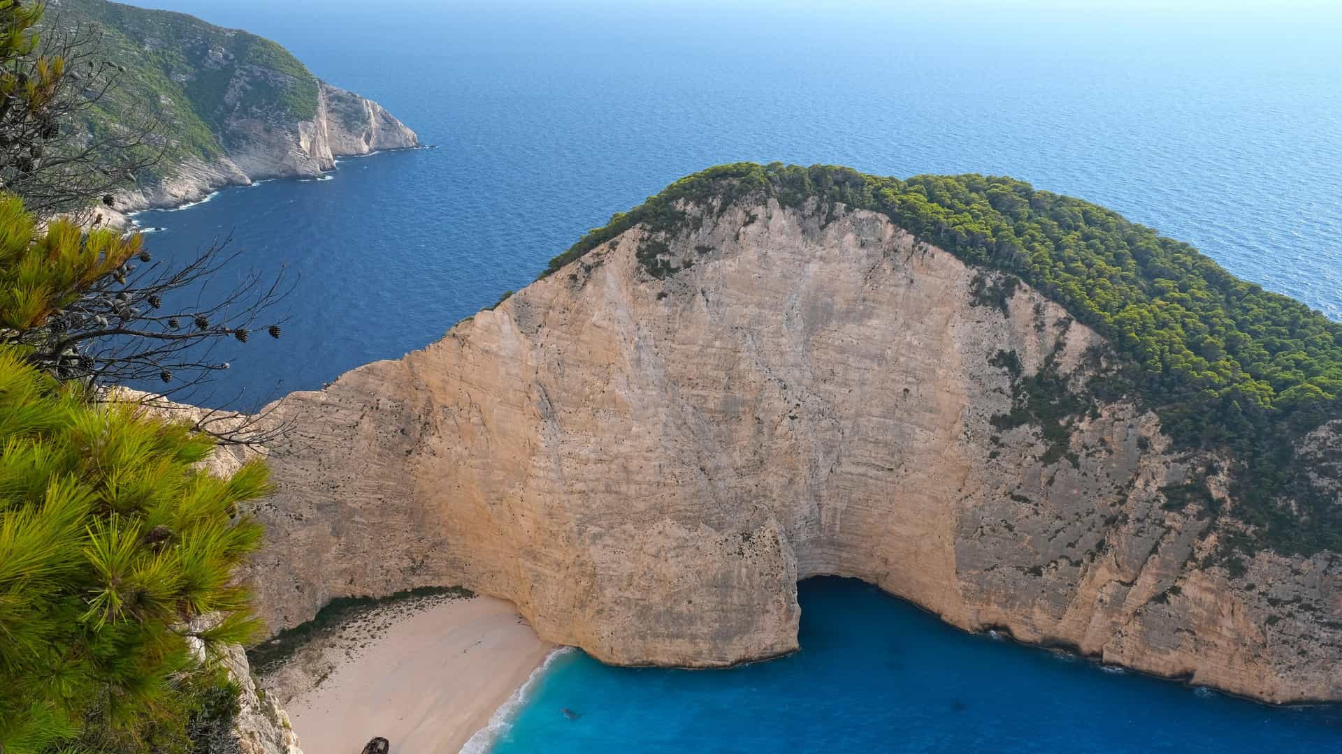 The iconic Navagio shipwreck beach on Zakynthos, Greece, seen from the clifftop, with the rusted shipwreck on white sand beneath towering limestone cliffs and turquoise Ionian water.