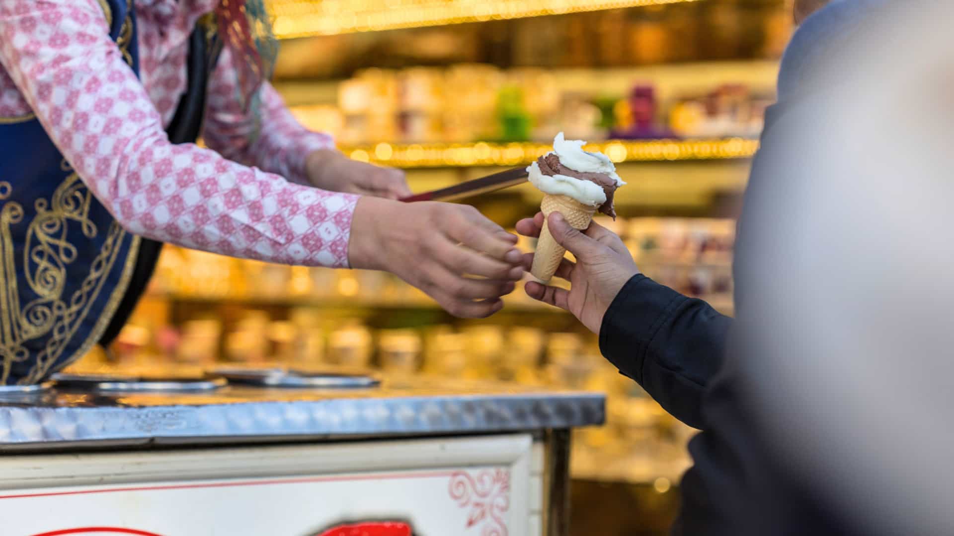 Close up of a Turkish man's extended arm holding and offering traditional Turkish ice cream to a customer.