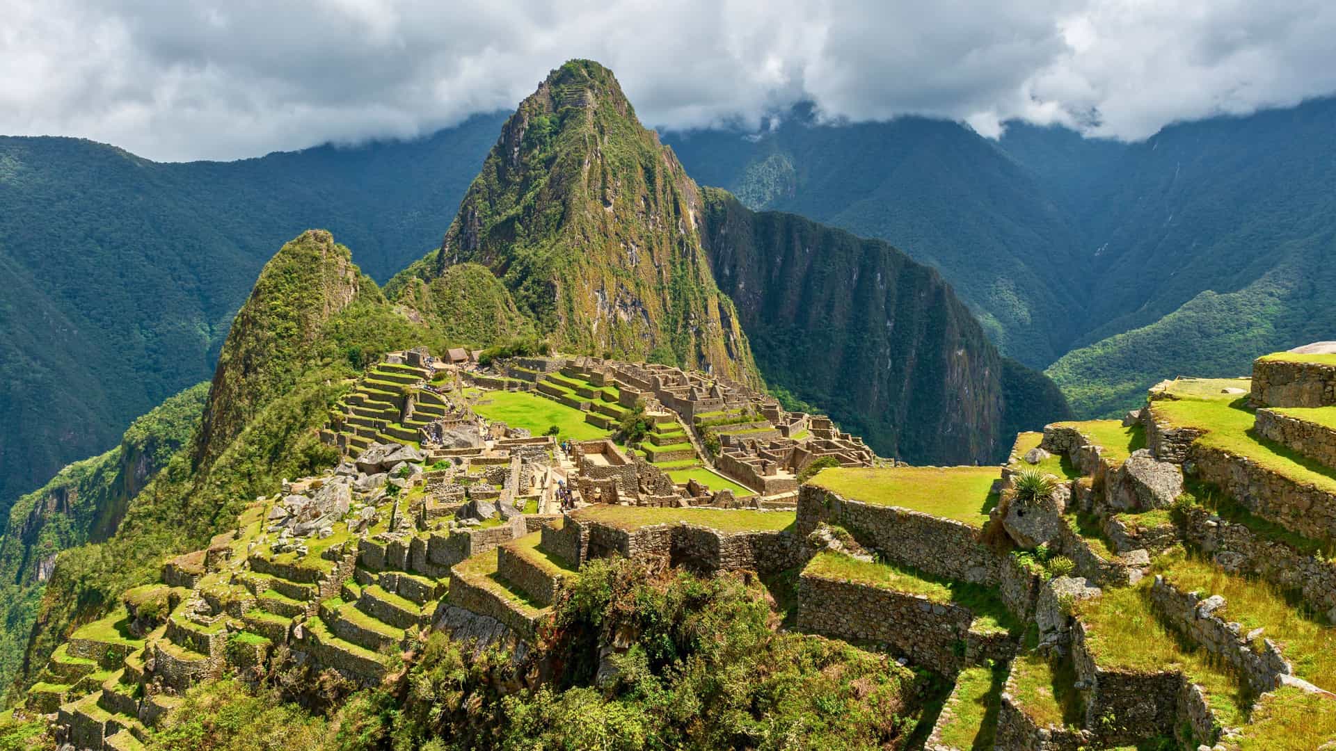 An aerial view of the ancient Inca citadel of Machu Picchu, with its stone ruins and terraced fields nestled between lush mountains, a monumental Uniworld river cruise destination in South America.