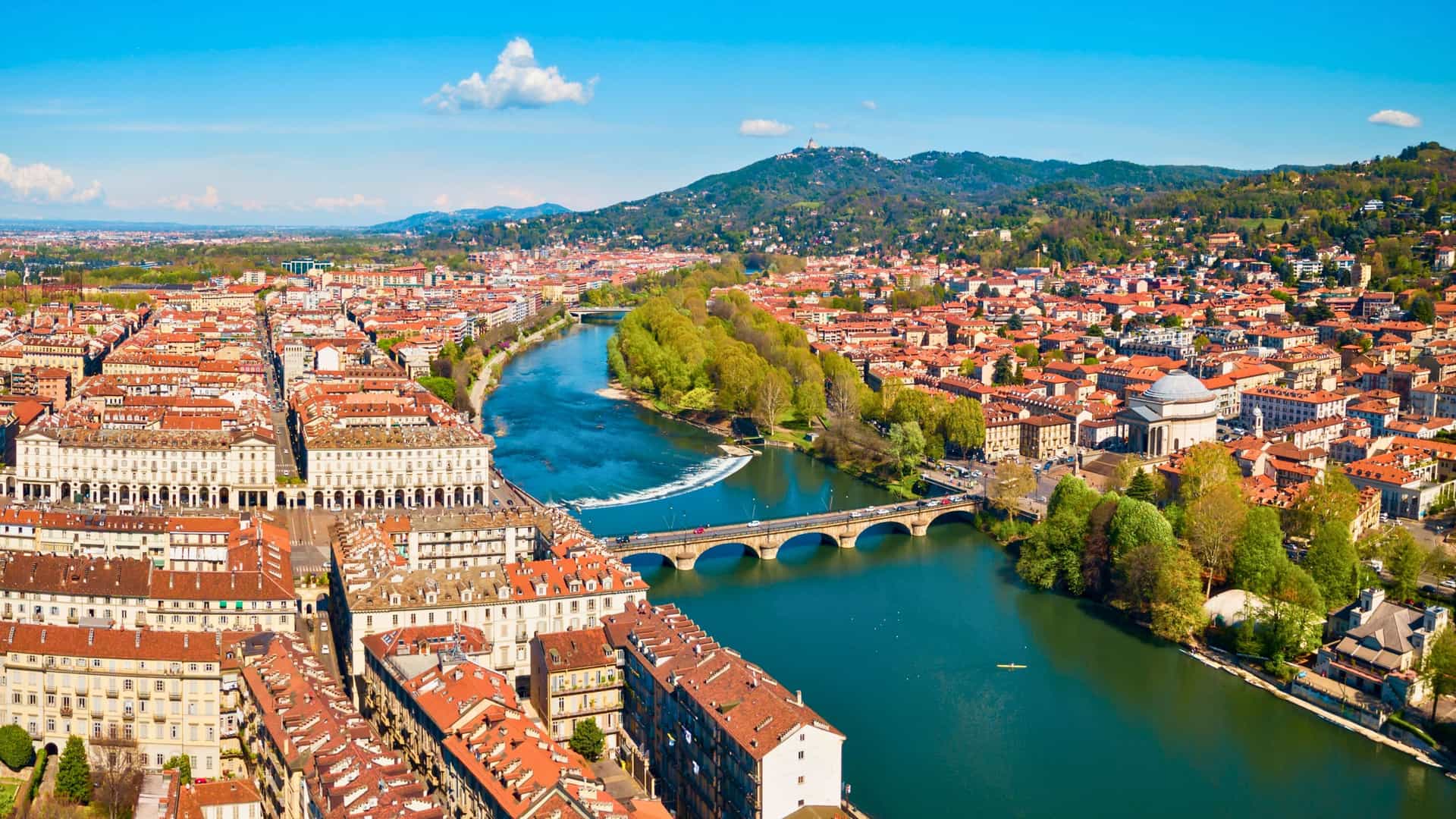 An aerial view of the Po River flowing through the city of Turin, Italy, with historic buildings and bridges visible under a clear blue sky, showcasing a beautiful Uniworld river cruise destination.