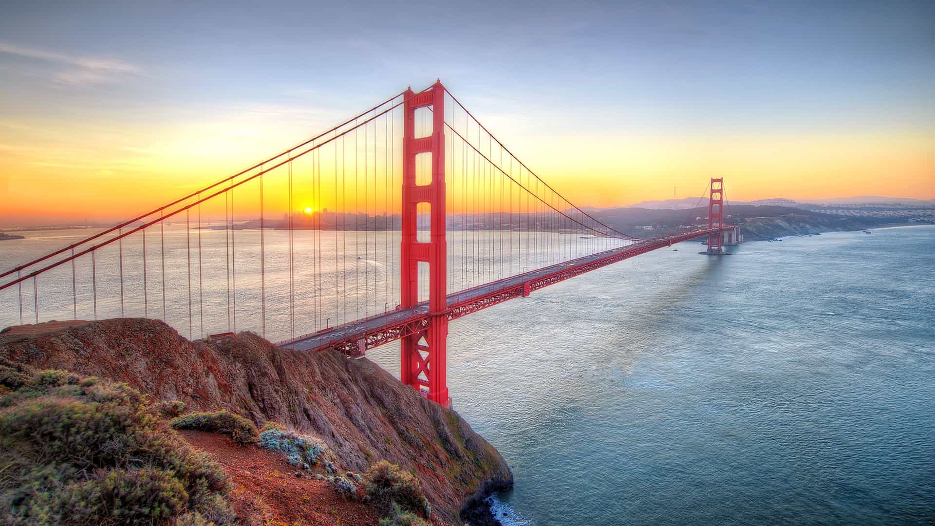 The Golden Gate Bridge silhouetted against a vibrant sunset sky, casting a warm glow over the water below