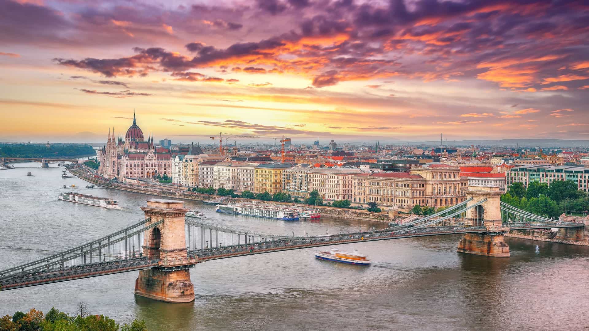 Sunset over a European city with a river and historic suspension bridge, highlighting a scenic stop on Viking Ocean Cruises' European river excursions.