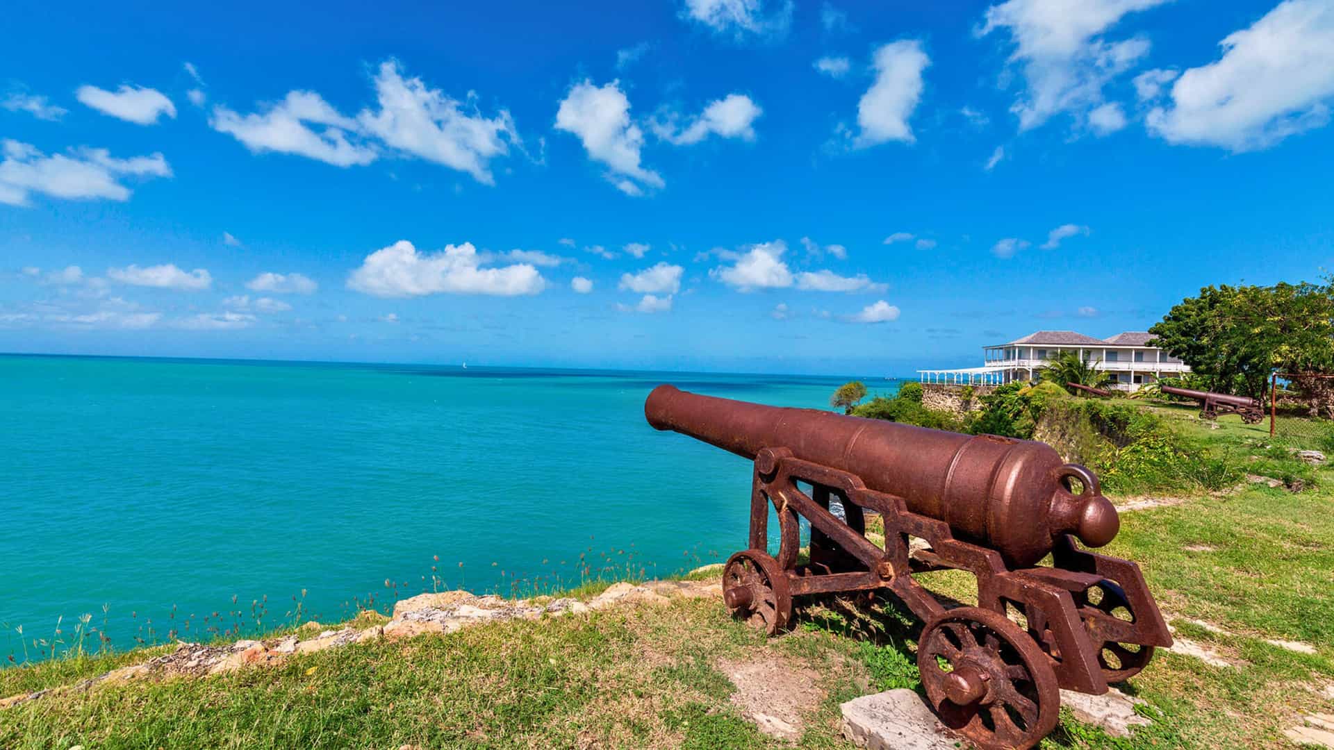 An old cannon overlooking the beautiful turquoise waters of English Harbour in Nelson's Dockyard, Antigua, a historic site and popular port of call for a Viking Ocean cruise to the Eastern Caribbean.