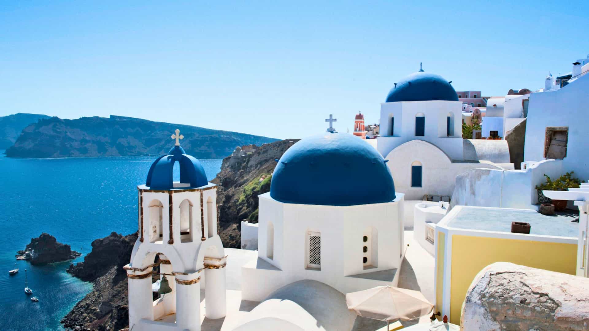 The iconic, blue-domed churches and whitewashed buildings of Oia, Santorini, Greece, with the Aegean Sea in the background, a popular stop on a Viking Ocean cruise to the Mediterranean.