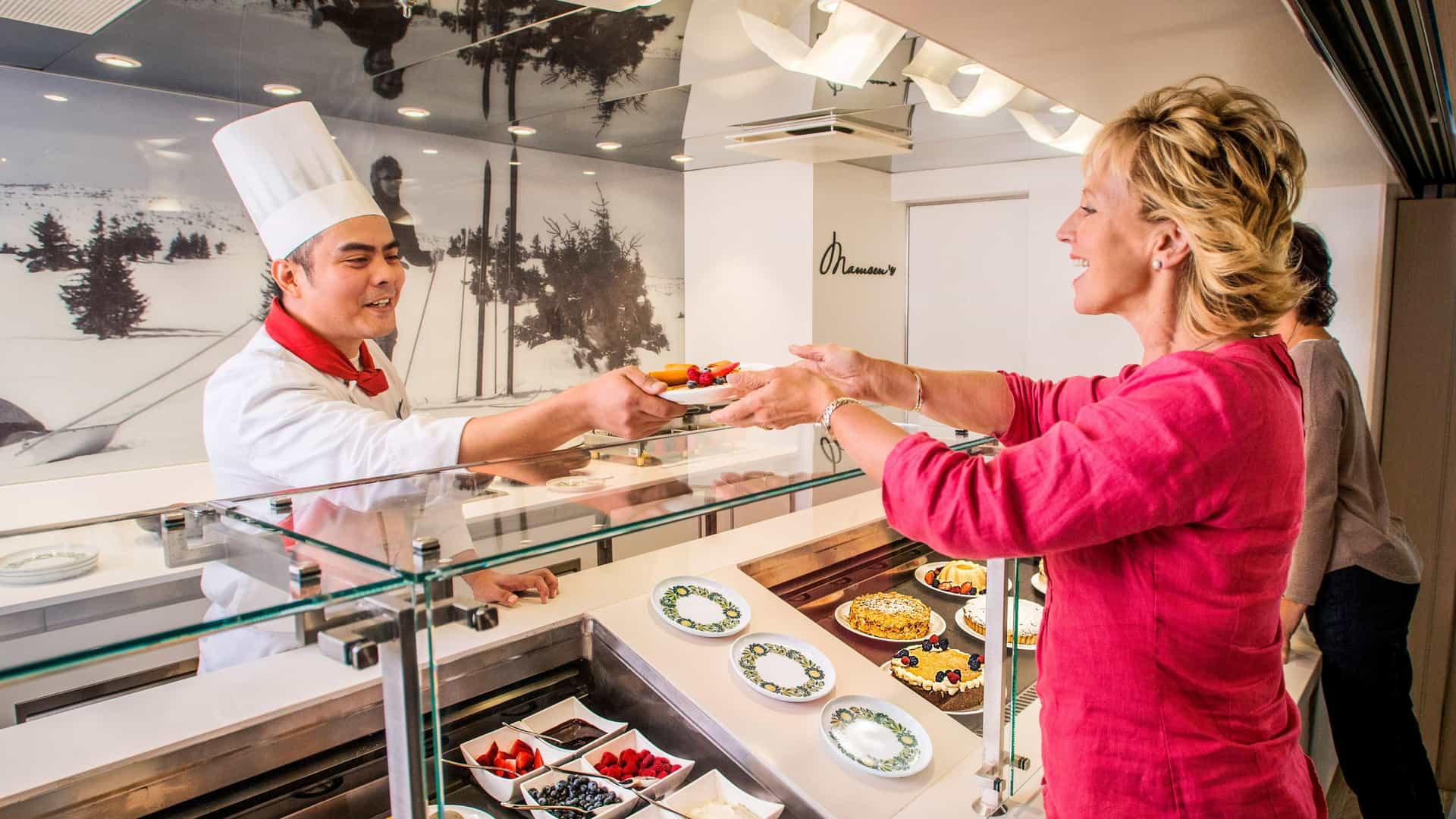 A shef at Viking Ocean's Mamsen dining venue, hands over a plate of fruit and waffles to a guest who happily accepts the plate.