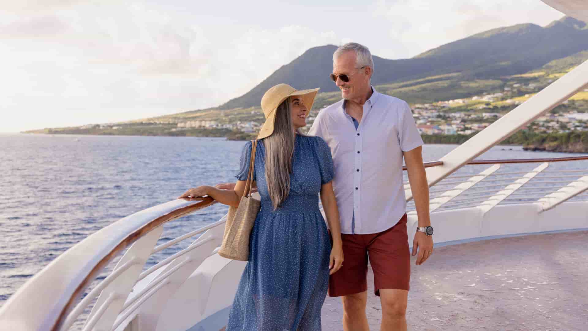 A happy couple enjoys the scenic view from the deck of a Windstar cruise ship during a luxury Caribbean vacation.