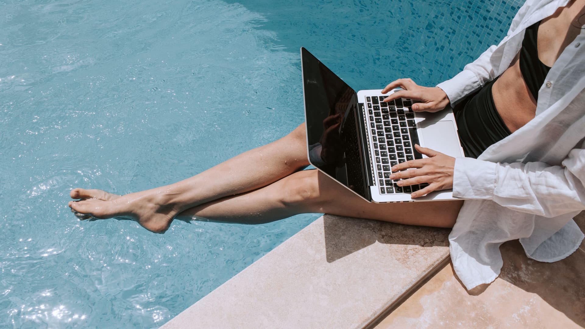 A woman sitting poolside utilizing the cruise ship's Wi-Fi to surf the web on her laptop.